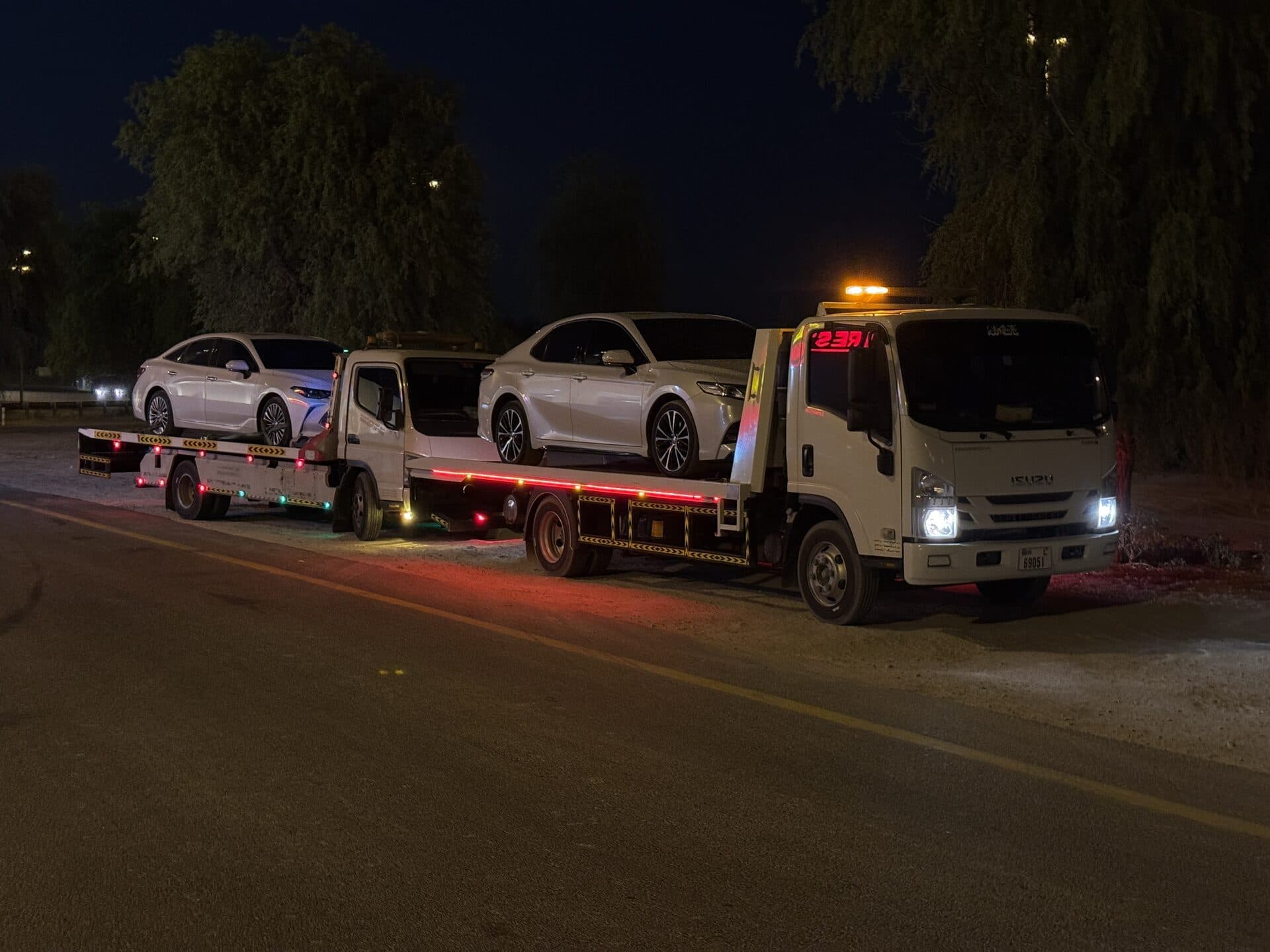 Two TAS Car Towing recovery trucks carrying sedans on a night recovery job in Dubai