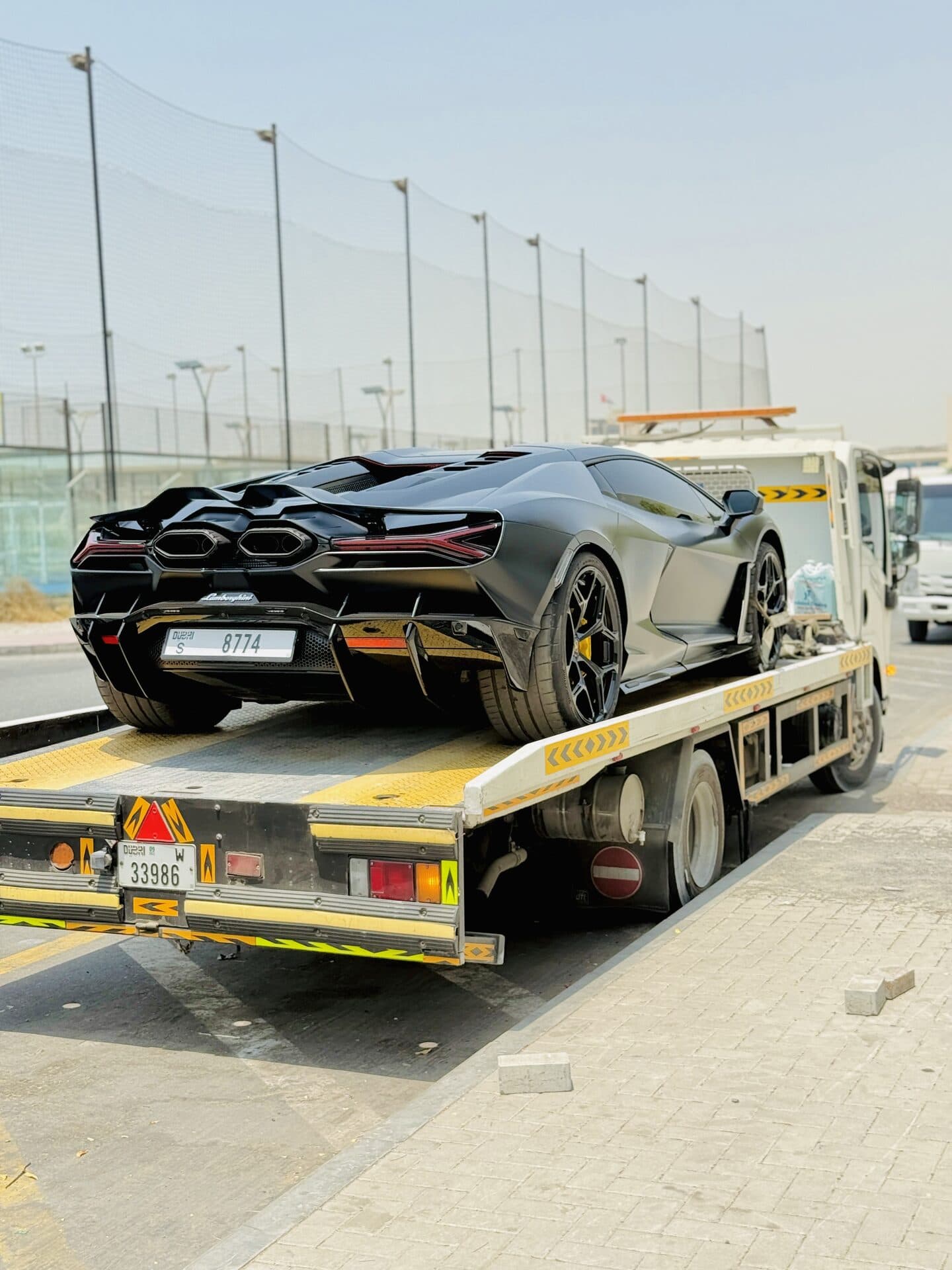 Rear view of a black Lamborghini Revuelto loaded on a TAS Car Towing flatbed truck