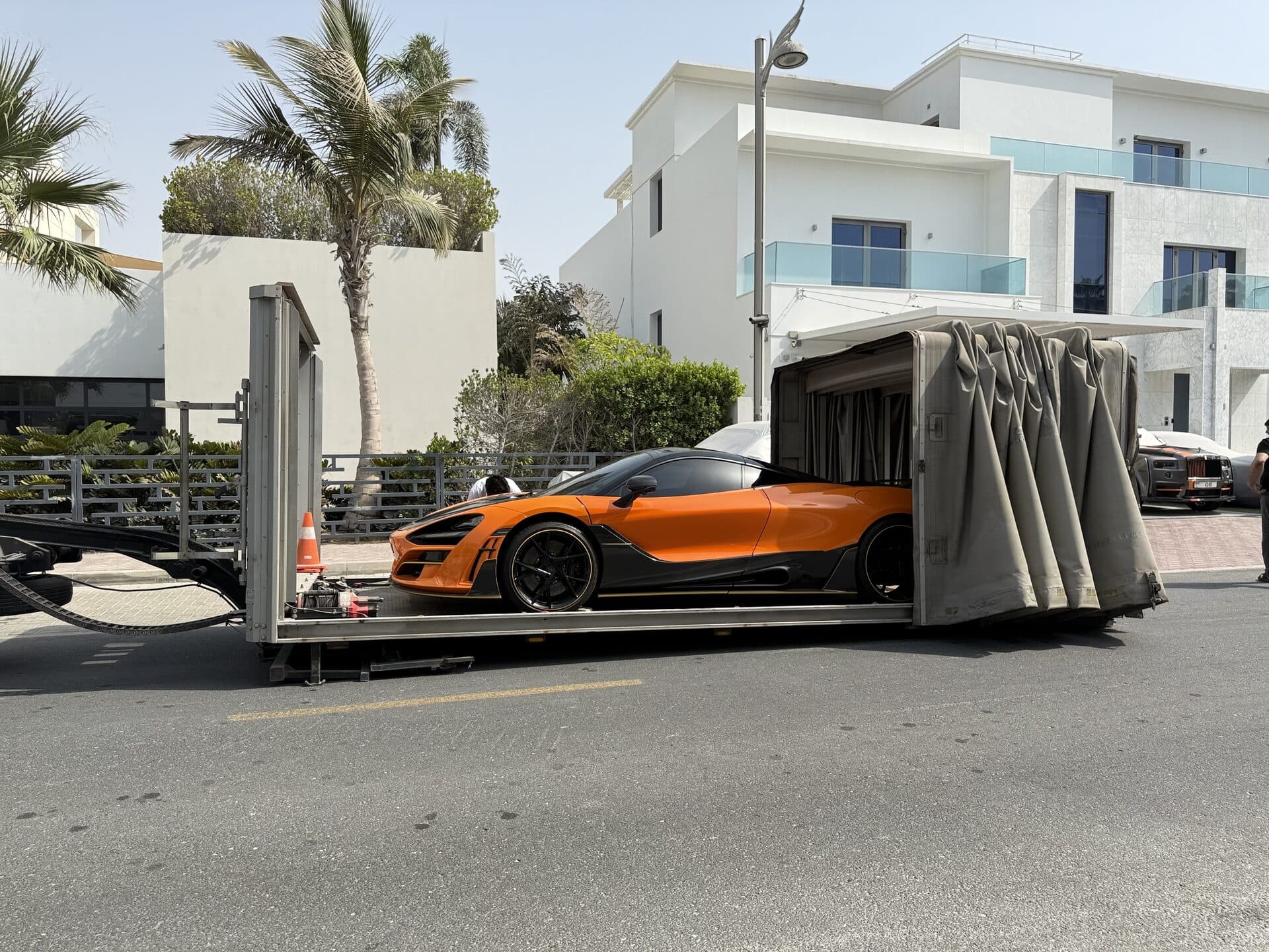TAS Car Towing enclosed flatbed trailer loading an orange McLaren supercar in Dubai